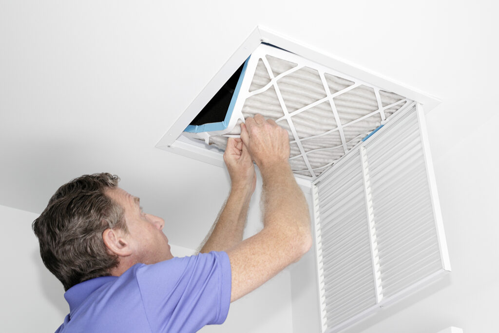 Technician removing dirty air filter from a white ceiling in a home.